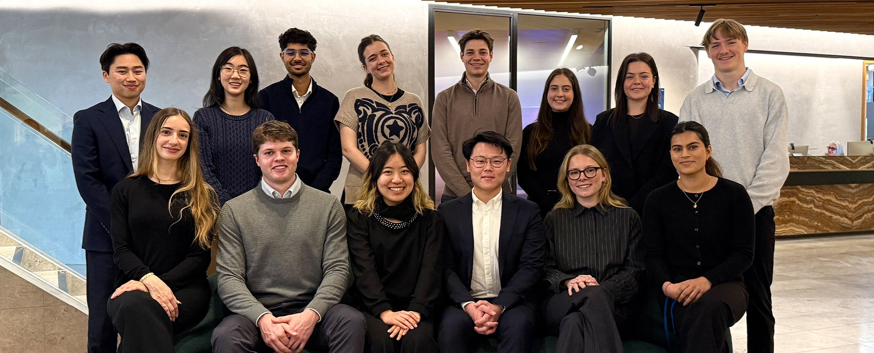 Group photo of our interns in business attire with some sitting and some standing in an office setting.